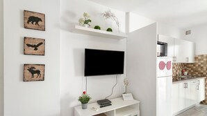 Una cocina moderna con muebles blancos, un televisor de pantalla plana sobre una consola blanca y decoración mural.