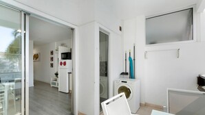 Un apartamento moderno con puerta de vidrio corredera que da a un balcón, lavadora y una peque ña cocina americana.