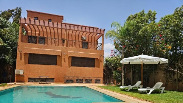 Ein zweistöckiges Gebäude mit Schwimmbad, überdachter Sitzgelegenheit und einem Garten mit Bäumen und Blumen.