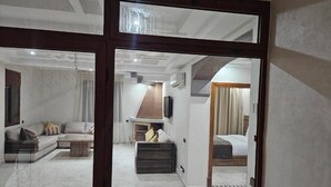 Ein modernes Hotelzimmer mit einer großen Schiebetür zu einem Wohnbereich, einem separaten Schlafzimmer mit einem Bett und einer kleinen Küchenzeile.