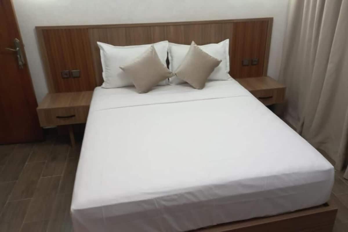 Ett hotellrum med en sänggavel i trä, ett vitt överkast, två sängbord och ett litet bord vid sängen i trä.