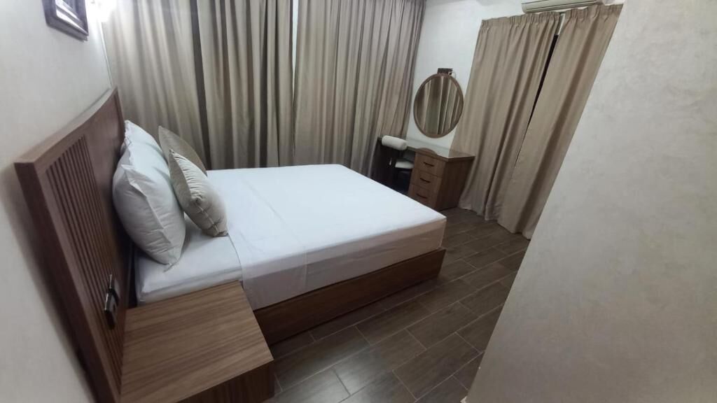 A bedroom with a wooden bed, a bedside table, a mirror, and a wardrobe.