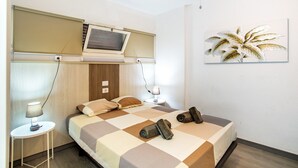 Una habitación de hotel con una cama, un televisor, una mesita con lámpara y una obra de arte colgada en la pared.