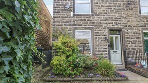 A stone house with a small garden, a white door, and a satellite dish. - Centenary Cottage (Skipton)