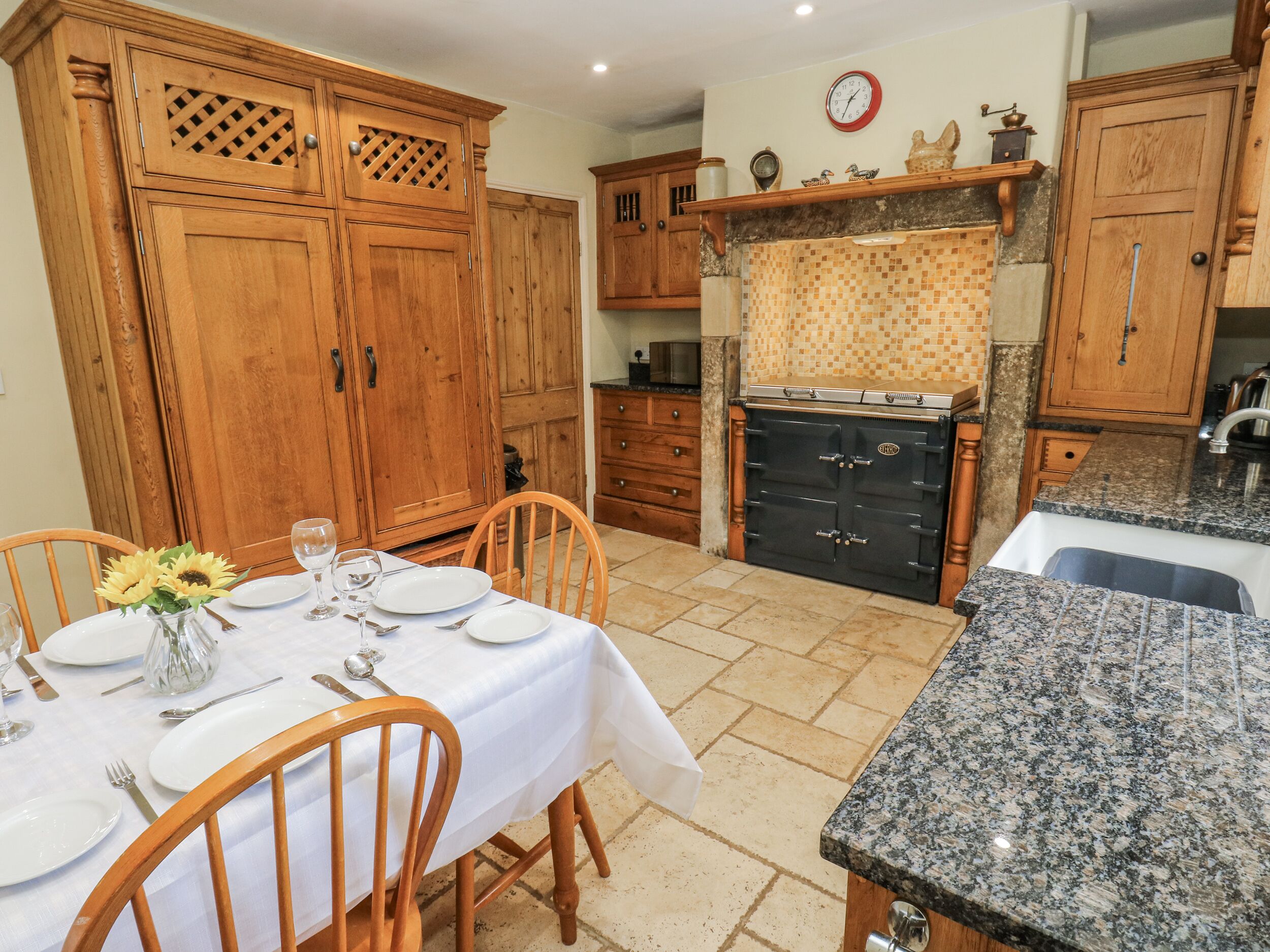 Een eethoek met een tafel voor vier personen, houten kastjes, een zwarte oven en een keukenblad.