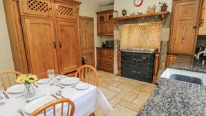 A dining area with a table set for four, wooden cabinets, a black oven, and a kitchen counter. - Centenary Cottage (Skipton)