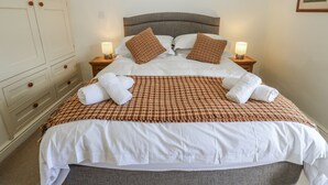 A neatly made bed with a checkered bedspread, two pillows, and two rolled towels. - Centenary Cottage (Skipton)