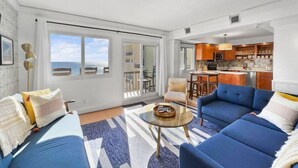 A spacious living room with a large sofa set, a coffee table, and a view of the ocean through large windows.