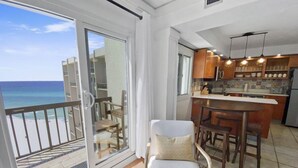 A balcony with a view of the ocean, a dining area with wooden furniture, and a kitchen with modern appliances.