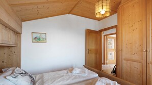 Une pièce avec un plafond en bois, un lit recouvert de draps blancs, une armoire en bois et un tableau encadré accroché au mur.