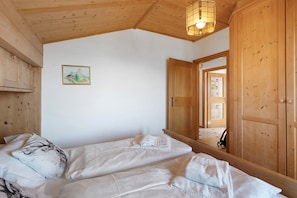 Une pièce avec un plafond en bois, un lit recouvert de draps blancs, une armoire en bois et un tableau encadré accroché au mur.