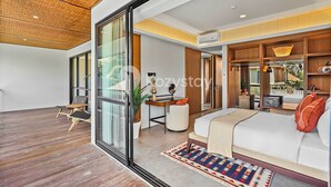 Una habitación de hotel moderna con un amplio ventanal corredero, techo de madera, cama con ropa blanca, escritorio con computadora y un pequeño espacio de descanso con sillas.