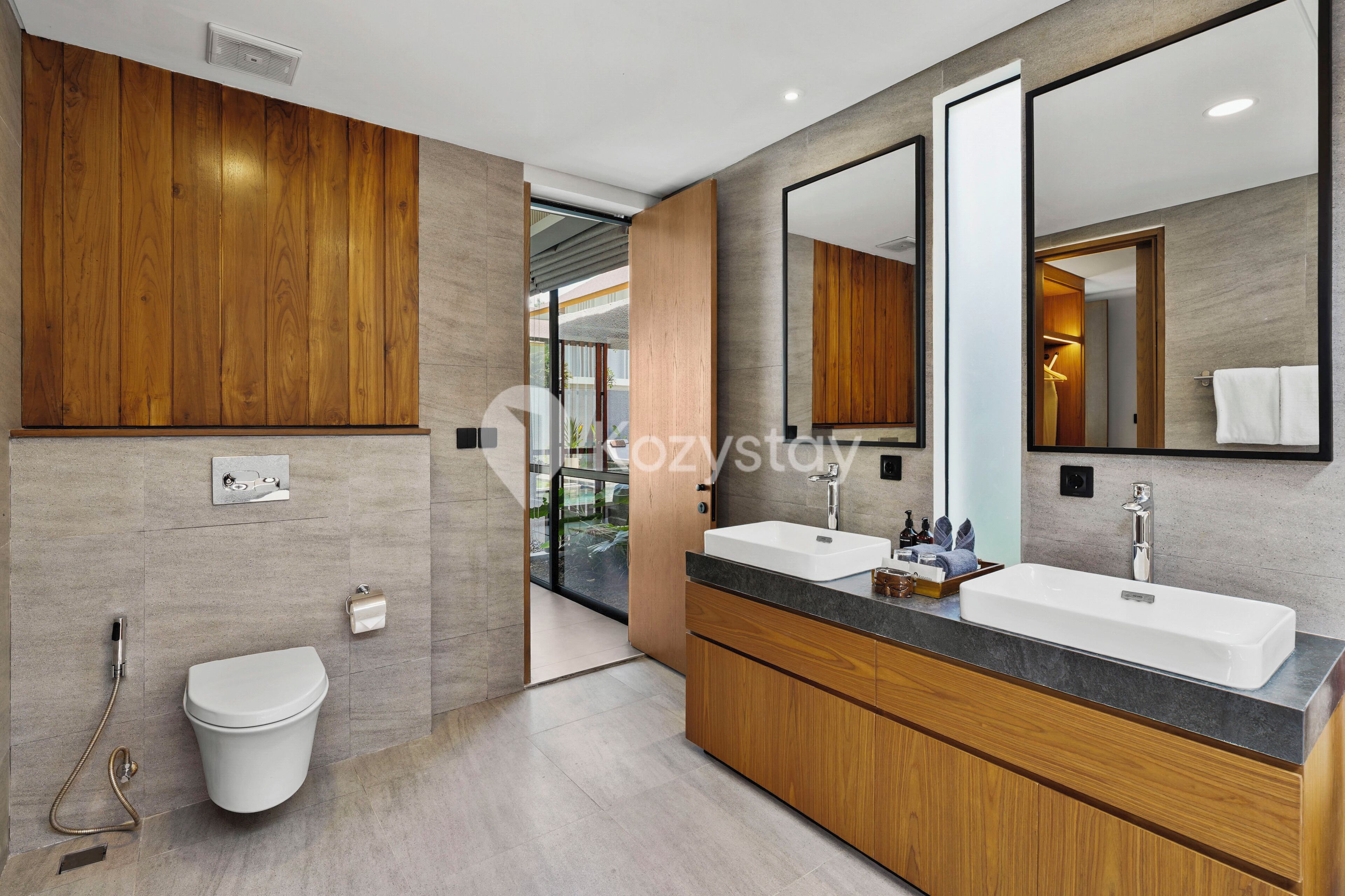 A modern bathroom with a wooden vanity, a large mirror, and a separate toilet.