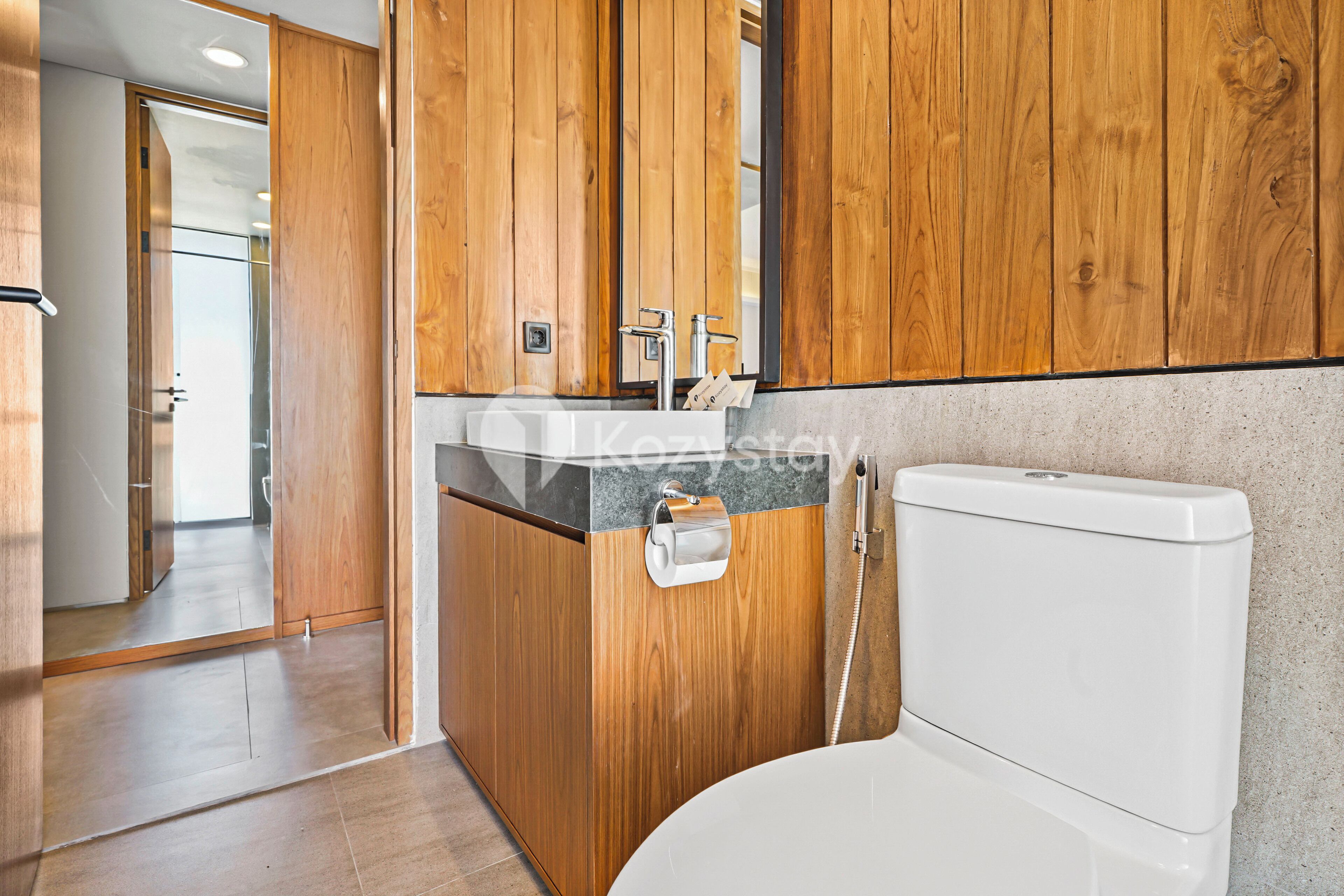 A modern bathroom with wooden cabinetry, a white toilet, and a glass shower enclosure.