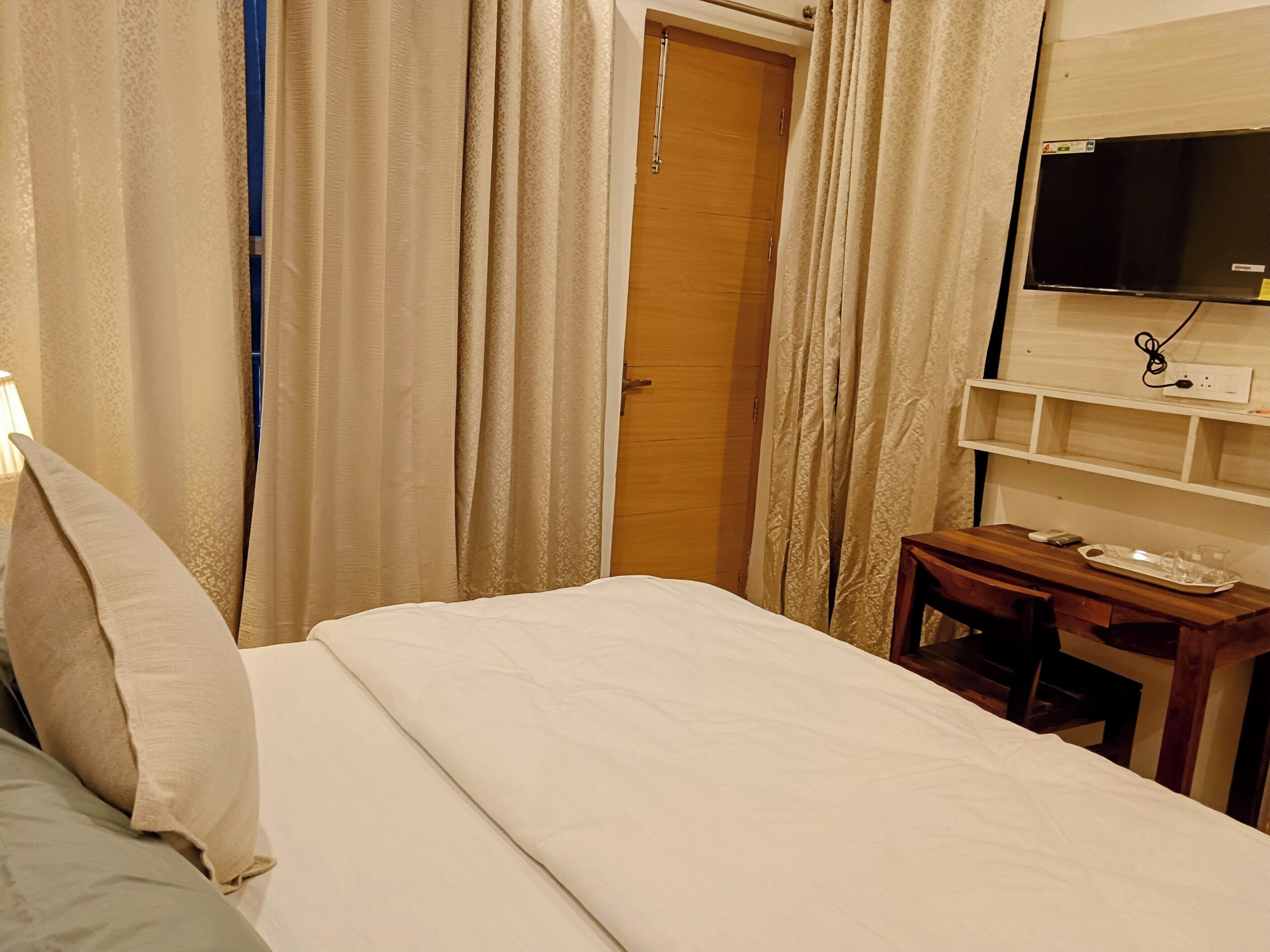 A hotel room with a bed, a desk with a chair, a television, and a wardrobe.