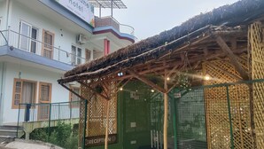 A hotel with a reception area, a covered outdoor seating area, and a sign indicating garden, pottery, and yoga services. - Pennylane Hotel (Rishikesh)