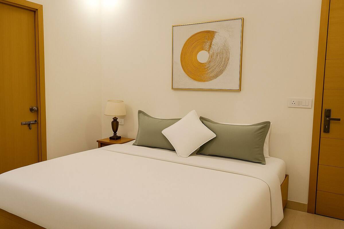 A hotel room with a bed, a nightstand with a lamp, a wall-mounted artwork, and a door.