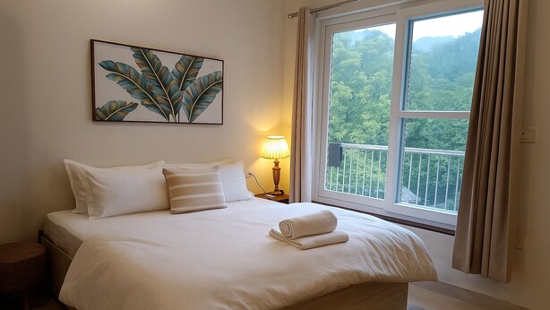 A neatly made bed with white linens, a bedside lamp, and a framed botanical print on the wall. - Pennylane Hotel (Rishikesh)