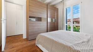 Un dormitorio con cama, armario de madera y ventana con vistas a edificios.