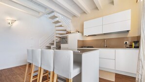 Una cocina moderna con armarios blancos, horno integrado y escalera de madera.