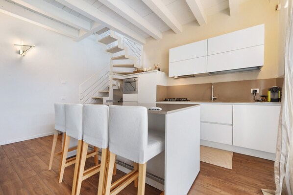 A modern kitchen with white cabinetry, a built-in oven, and a wooden staircase.