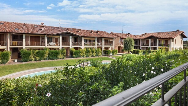 Un hotel con varios balcones, piscina y abundante vegetación.