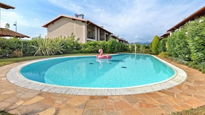Una piscina con un flotador de flamenco, rodeada de baldosas de piedra y follaje.