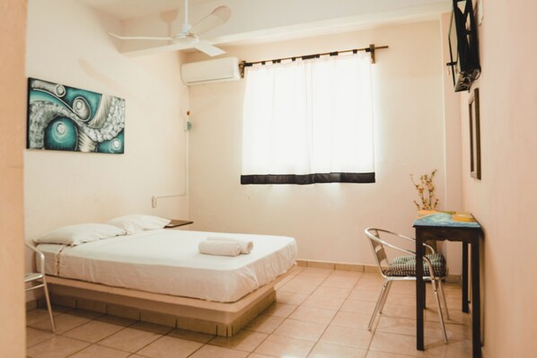 A bedroom with a bed, a chair, a desk, a ceiling fan, and a window with curtains. - Lifestyle Hotel Juquilita (Puerto Escondido)