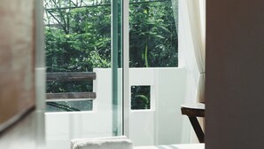 A bedroom with a bed, a view of greenery outside through large windows, and a chair near the window. - Lifestyle Hotel Juquilita (Puerto Escondido)