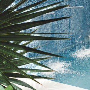 A pool with a waterfall feature, surrounded by palm leaves.