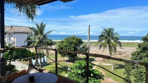 A balcony with a view of the ocean, a thatched roof, and a white building with a balcony. - Lifestyle Hotel Juquilita (Puerto Escondido)