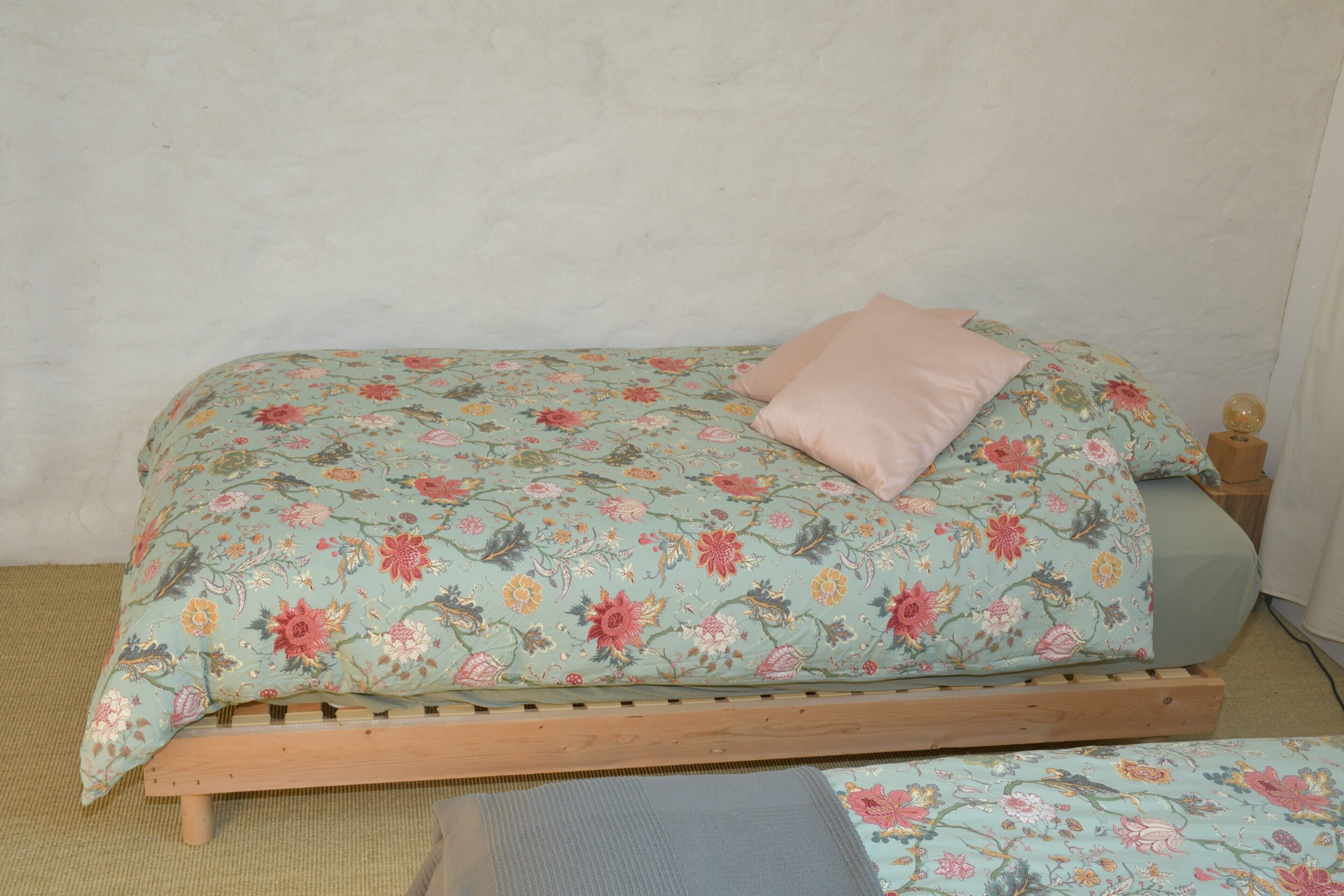 A bed with a floral bedspread and a single pink pillow.