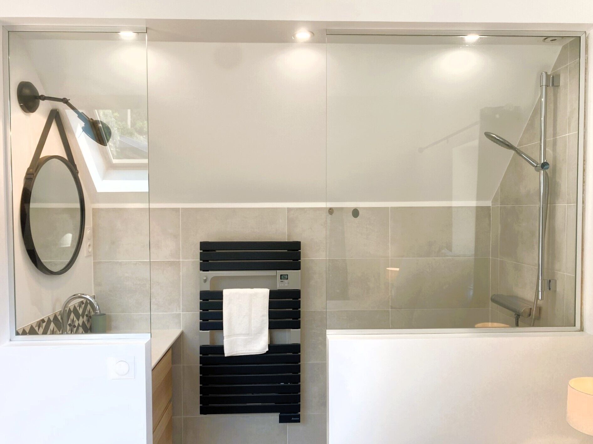 A modern bathroom with a glass-enclosed shower, a black towel rack, a mirror, and a sink with a patterned backsplash.