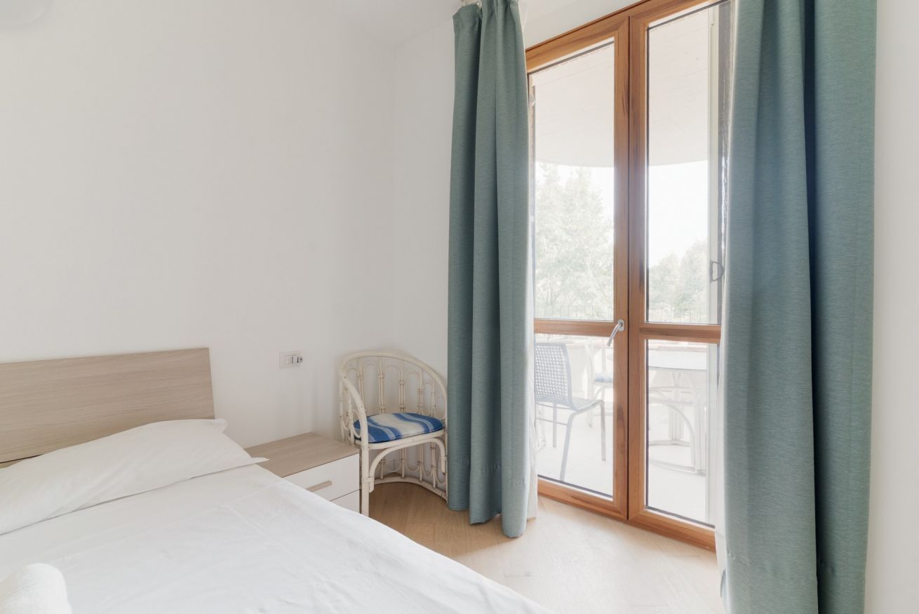 A bedroom with a bed, a chair, a small table, and a sliding glass door leading to an outdoor area.