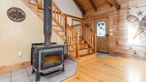 A cabin interior with a wooden staircase, a fireplace, and a door with a decorative angel.