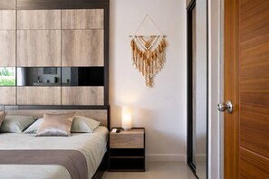A bedroom with a bed, bedside table, lamp, and a macrame wall hanging.