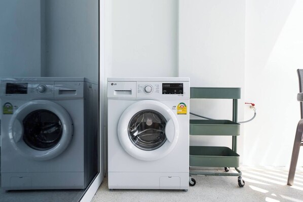 Two front-loading washing machines side by side in a laundry room with a green cart and a wall-mounted water faucet.