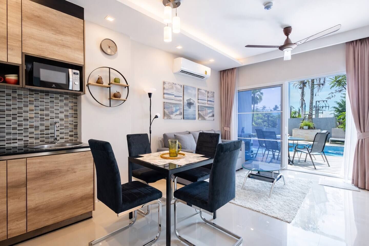 A modern kitchen with a microwave, a dining table with chairs, and a view of a swimming pool through large windows.