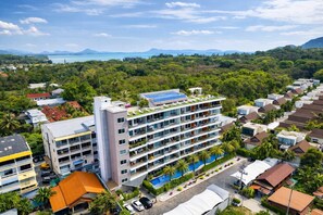 A multi-story hotel with a rooftop pool, surrounded by lush greenery and a view of the sea. - Condo Vireo | Pool View | Rawai (Tambon Rawai)