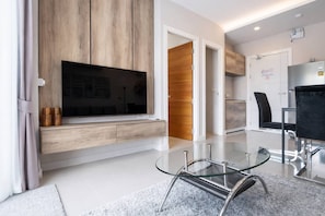 Un salon moderne doté d’un téléviseur à écran plat, de lambris en bois, d’une table basse en verre et d’un coin salon avec un fauteuil.