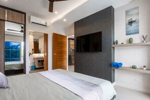 Quarto moderno com cama, TV fixada na parede e vista para o exterior pela janela.