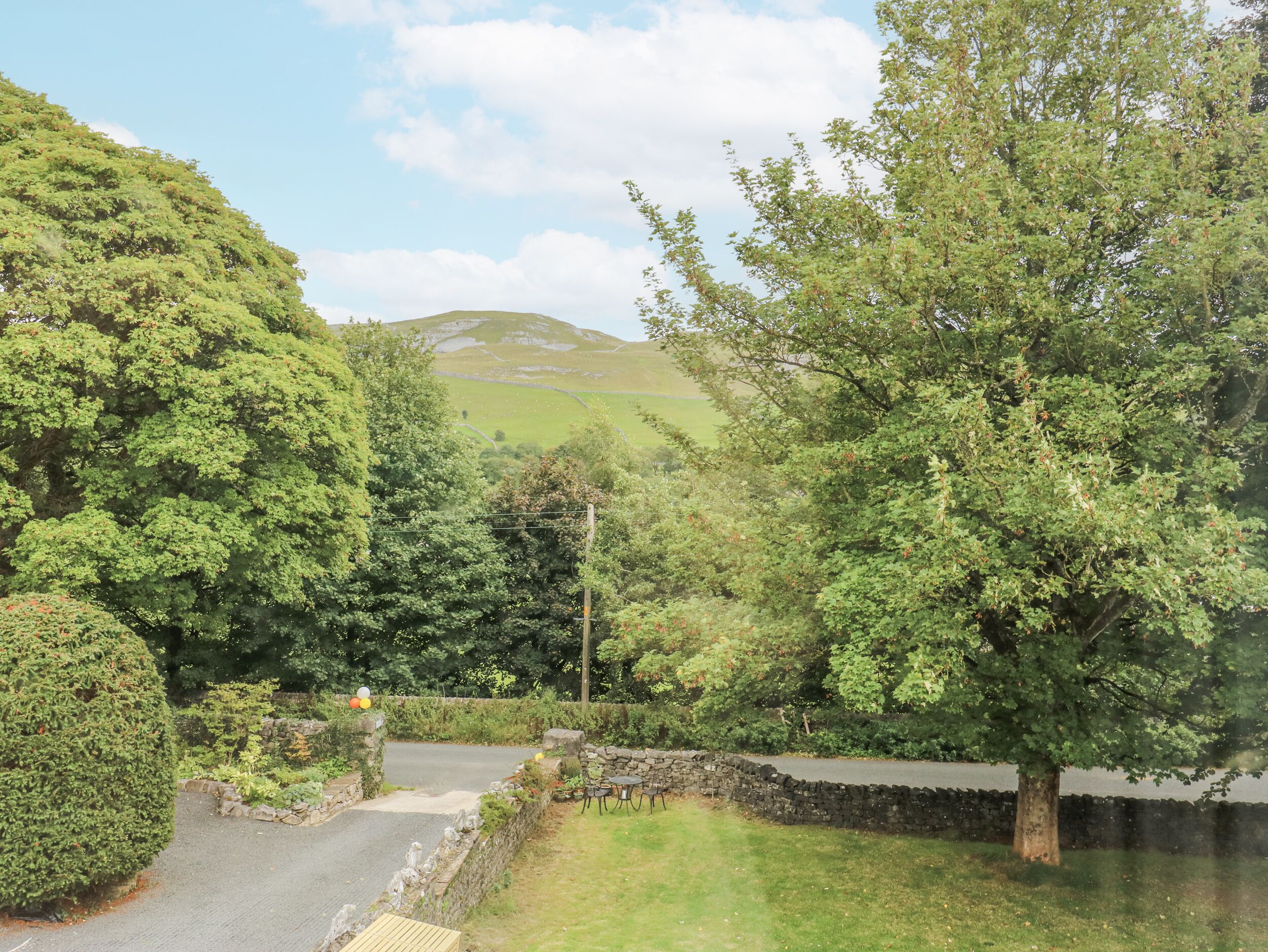 A rural landscape with a stone wall, a paved path, and a grassy area with trees.