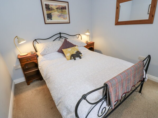A neatly made bed with a white duvet, two bedside lamps, a small bedside table with a lamp, a framed picture on the wall, and a mirror.