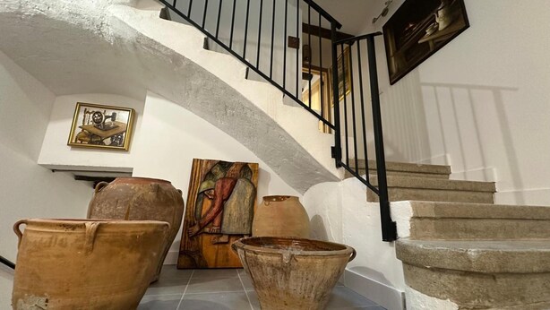 Una escalera con barandilla negra, macetas de terracota y un cuadro enmarcado en la pared.