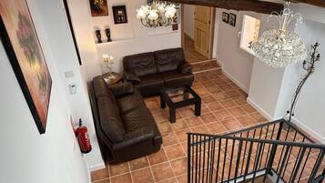 A living room with a brown leather sofa, a glass coffee table, a chandelier, and a staircase with a metal railing.