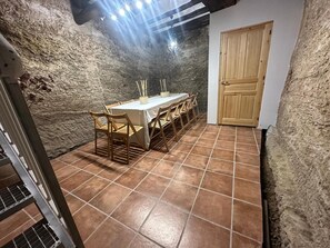 A dining area with a table set for six, surrounded by stone walls and a wooden door.