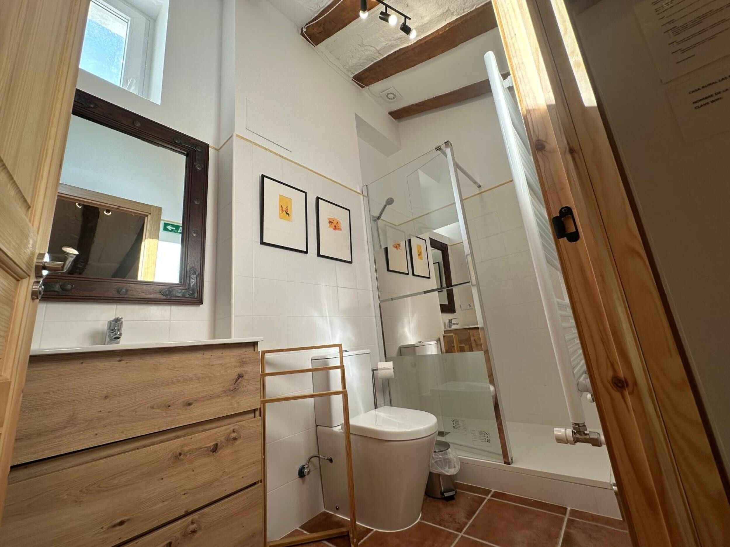 A bathroom with a wooden vanity, a toilet, a glass shower enclosure, and framed pictures on the wall.