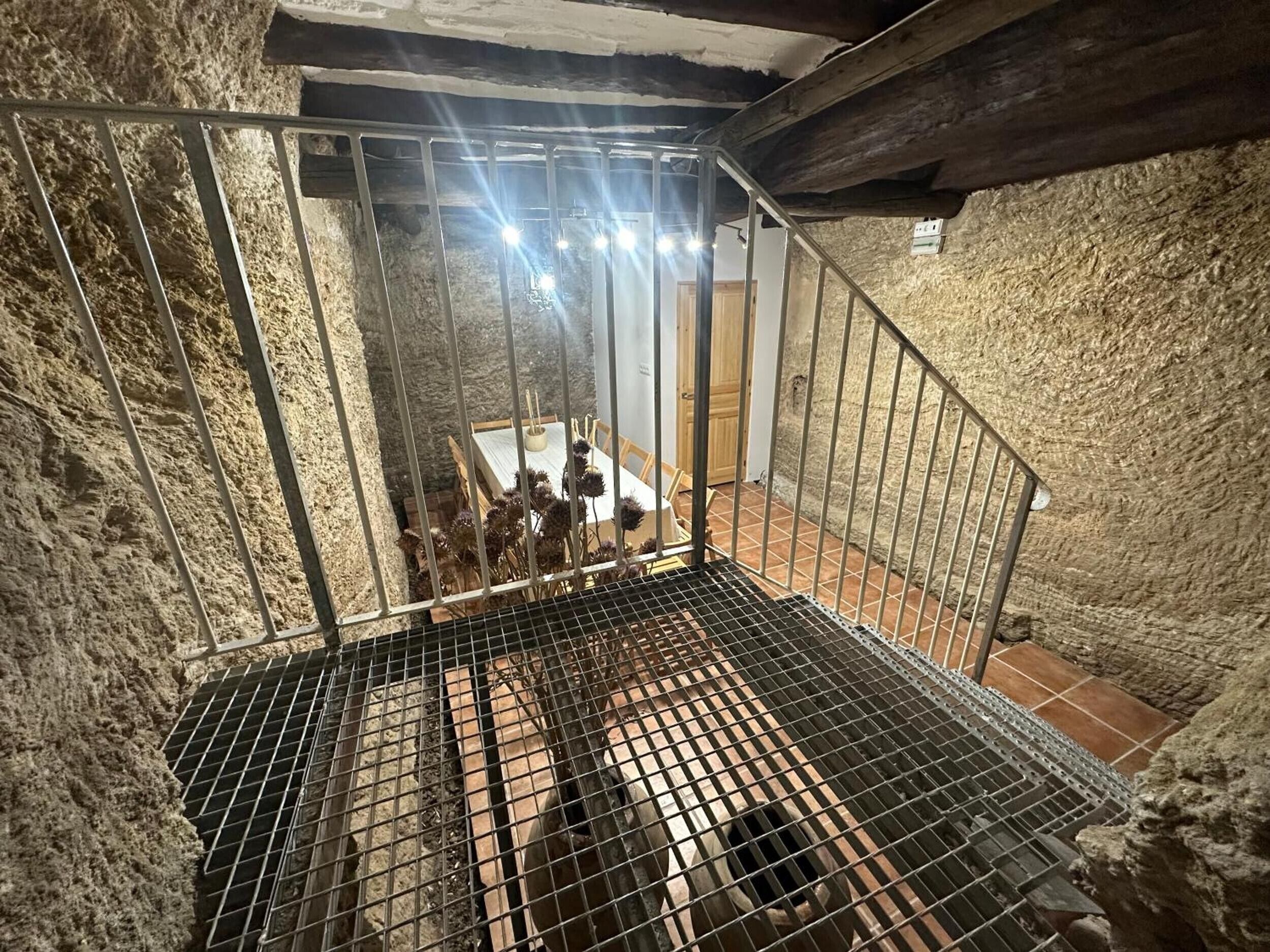Eine Metalltreppe mit Metallgeländer führt zu einem Raum mit gefliestem Boden und einem Tisch mit Stühlen.