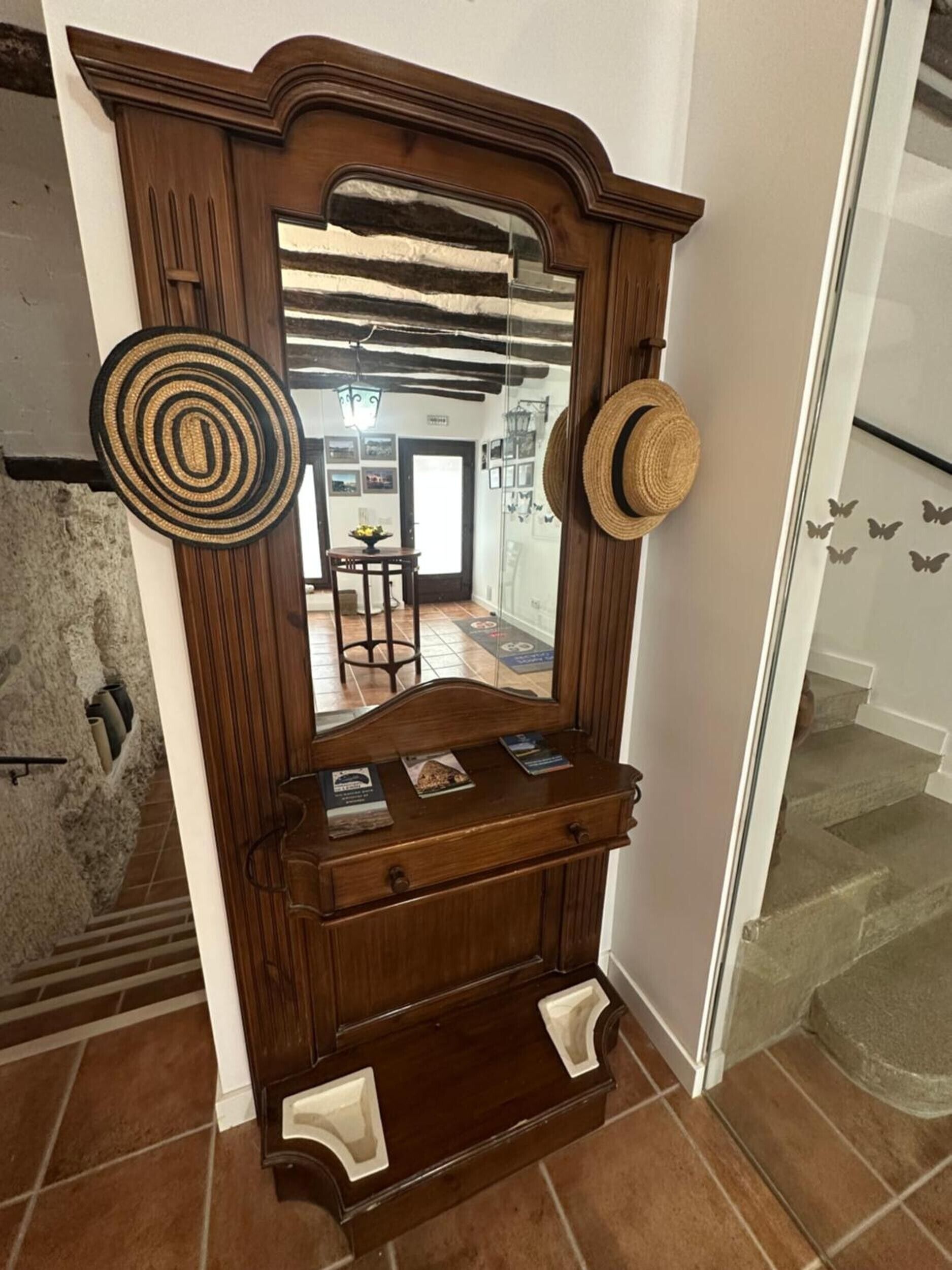 A wooden mirror with a decorative frame, a small shelf with books, and two hats hanging on the wall.
