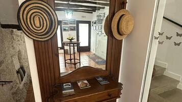 A wooden mirror with a decorative frame, a small shelf with books, and two hats hanging on the wall.